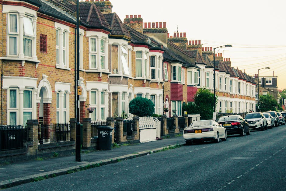 A row of Victorian-style terraced houses with decorative white ironwork on their small front porches and balconies, set against a bright blue sky. The buildings feature brick facades with pointed gabl
